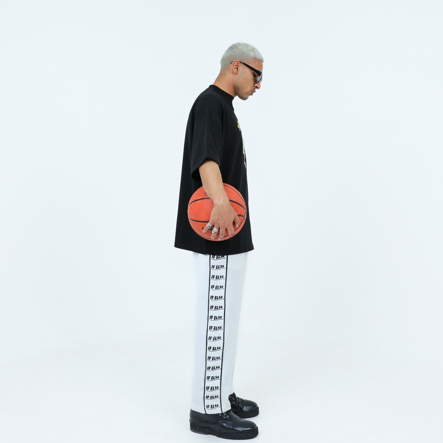 Person wearing a black oversized t-shirt and printed pants, standing sideways holding a basketball.