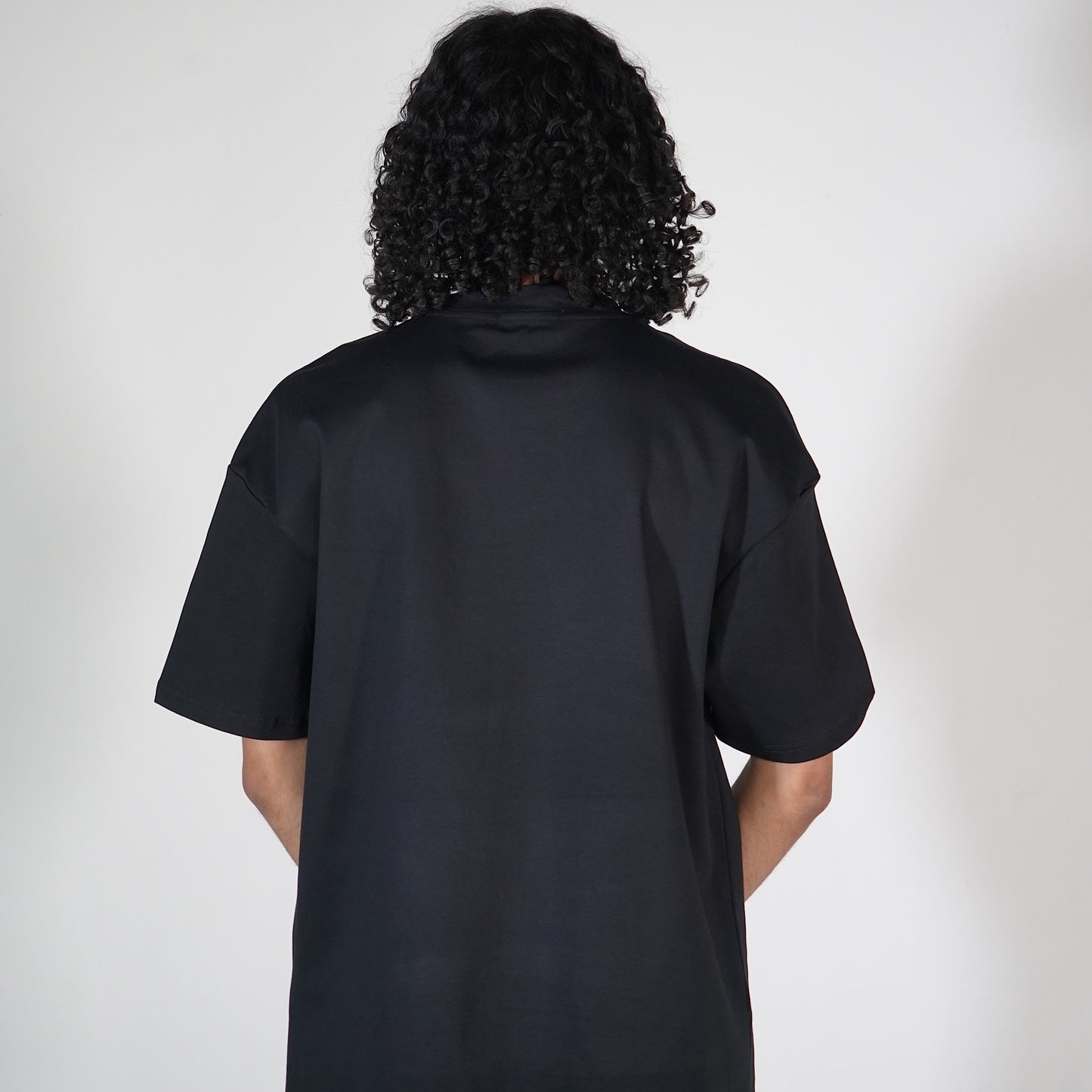 The back view of a person with curly hair wearing a plain black t-shirt.
