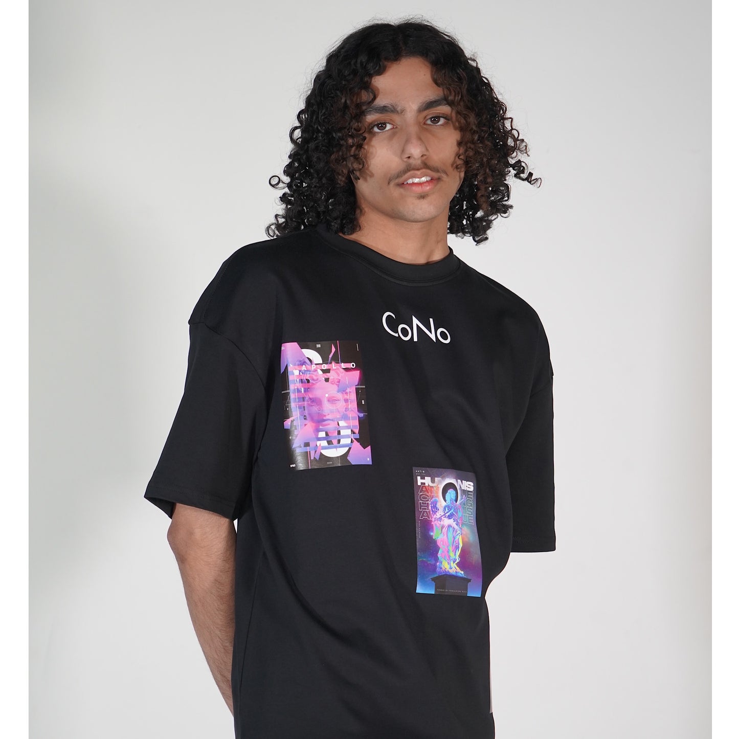 A person with curly hair facing left, showcasing a black t-shirt with a colorful graphic design on the front.